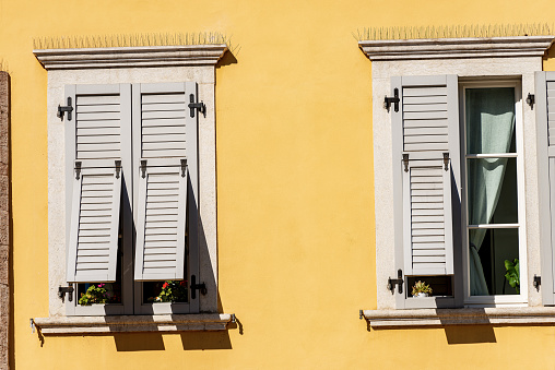 Two windows with grey wooden shutters with spike steel sticks to prevent birds from stopping, especially pigeons, residential building in Trentino, Italy, Europe