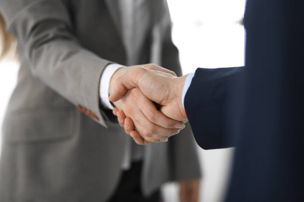 istock Business people shaking hands while standing with colleagues after meeting or negotiation, close-up. Group of unknown businessmen and women in modern office. Teamwork, partnership and handshake concept, toned picture 1217735716