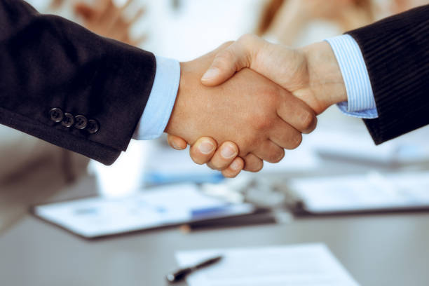 istock Business people shaking hands at meeting while theirs colleagues clapping and applauding. Group of unknown businessmen and women in modern white office. Success teamwork, partnership and handshake concept 1217736236