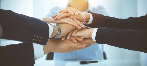 Photo of Business team showing unity with their hands together in sunny office. Group of people joining hands and representing concept of friendship, teamwork and partnership