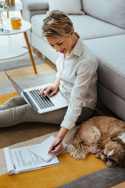 Happy businesswoman writing notes while working on a computer at home.