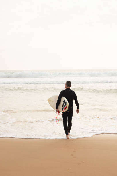 istock Back view of middle-aged surfer entering water sea 1217740437