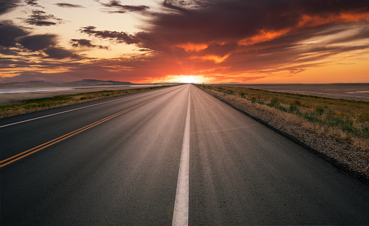 Straight asphalt road running to the horizon at sunset