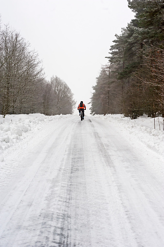 Cyclist riding on remote snow covered road going into the distance through trees