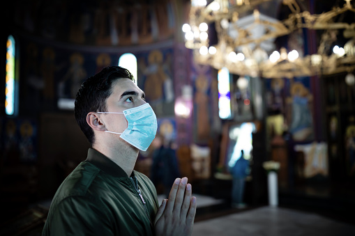 Concept, diseases, viruses, allergies, air pollution. Portrait of young man wearing protective mask, in church. The face of a young man wearing a mask to prevent germs, toxic fumes and dust. Prevention of bacterial Corona virus infection or Covid 19 in the air around streets and gardens.