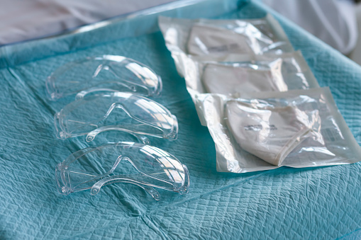 Three plastic protective eyeglasses  and three respirators ffp2 on table in ICU in hospital, personal protective equipment to protect against the virus covid-19.