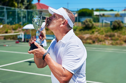Cropped shot of a handsome mature man standing and kissing his trophy after winning a tennis match during the day