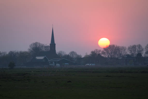 Classic view of a colorful sunset over a traditional dutch village with church tower.