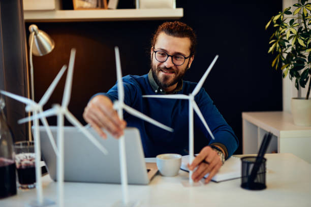 istock Young innovative dedicated bearded employee sitting in his modern office and drawing sketches of windmills. Sustainable development concept. 1217757536