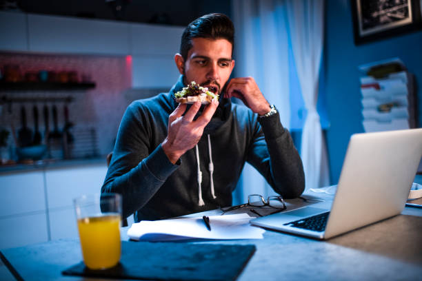 istock Young male having a sandwich while working from home on his laptop 1217758593