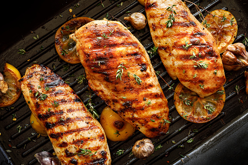 Grilled chicken breasts with thyme, garlic and lemon slices on a grill pan close up, top view