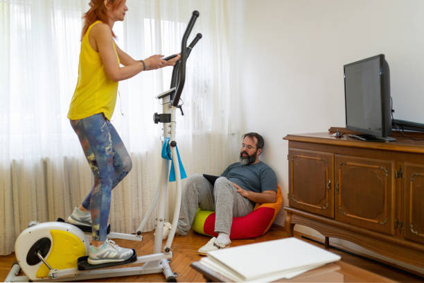 istock Woman exercising on elliptical trainer while her partner is using digital tablet in the living room 1217763825