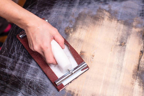 hand with a carpentry holder for sandpaper erases and polishes an old wooden surface, prepares for painting. home repairs. - carpenter restoring furniture wood imagens e fotografias de stock