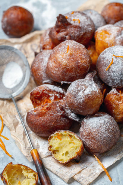 French beignets with powdered sugar and orange zest. Homemade French doughnuts Beignet with orange zest and powdered sugar on parchment paper, selective focus. beignet stock pictures, royalty-free photos & images