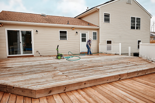 Latin woman cleaning wooden terrace with a high water pressure cleaner.