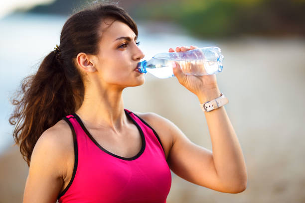 istock Young girl athlete drinks water on the beach. 1217790656