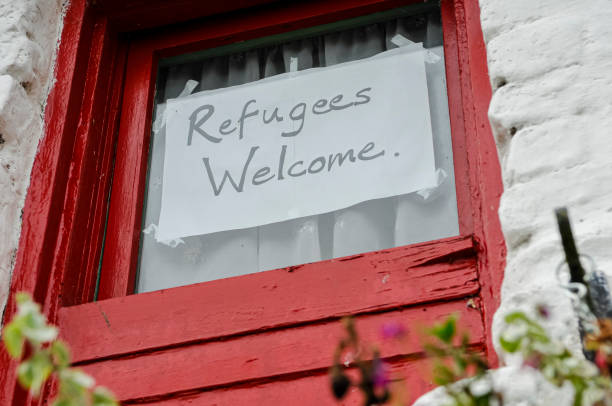 A handwritten "Refugees Welcome" sign taped to a window with a red wooden frame on a white building.