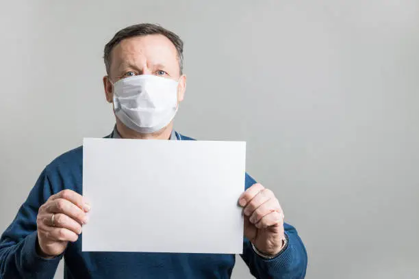 Photo of Adult man in protective medical mask holding white blank for text.