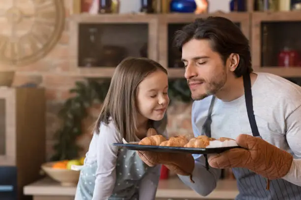 Photo of Homemade pastries. Cute little girl and dad smelling freshly baked croissants
