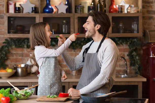 istock Girl and her father feeding each other with vegetables while cooking 1217793941
