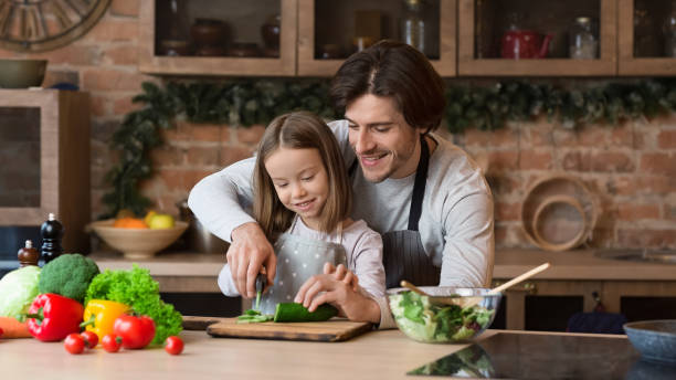 istock Daddy Teaching Little Daughter How To Use Knife In Kitchen 1217793992
