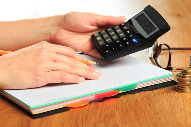 female hands working on a calculator on wooden background  - Image