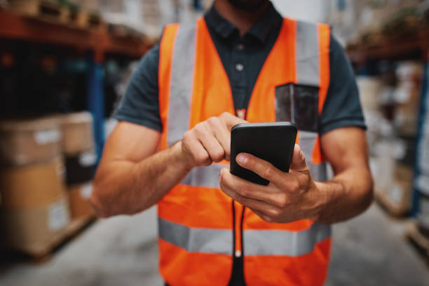 istock Closeup of man hands using mobile phone while in warehouse in uniform 1217794617