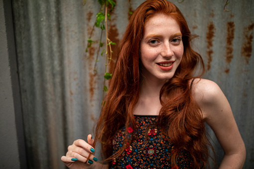 Beautiful redhead woman with freckles standing in front of rusty garage doors,looking at camera and smiling