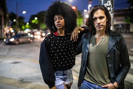 Portrait of young hipster couple on the street at night, beautiful woman with Afro hair and man with long hairstyle