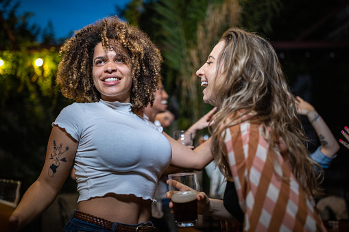 Multi-ethnic group of friends drinking beers, dancing and enjoying weekend at outdoors nightclub
