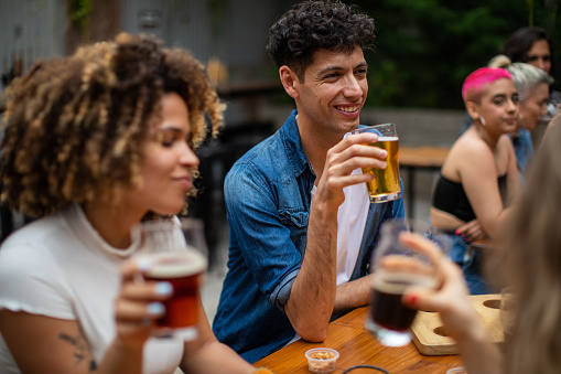 Multi-ethnic hipster friends drinking beer and enjoying beautiful day together at outdoor pub