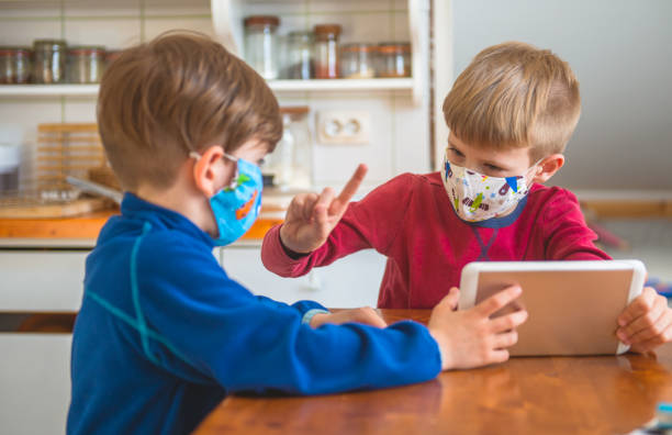 istock Boys Playing With Digital Tablet At Home, Wearing Protective Masks 1217801275