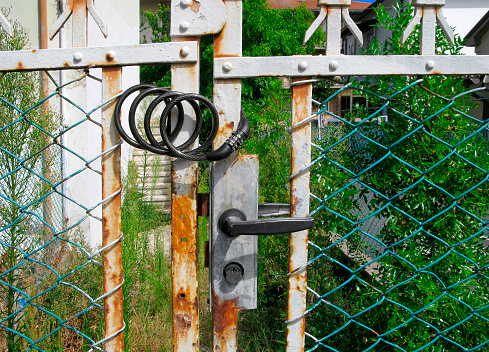 The door on the old fence is additionally locked with a flexible cable lock with a code. Combination lock close-up. Security protection padlock.