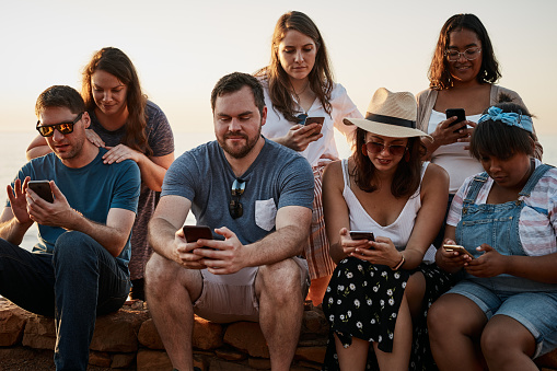 Cropped shot of a group of young friends using their smartphones while sitting together at the beach