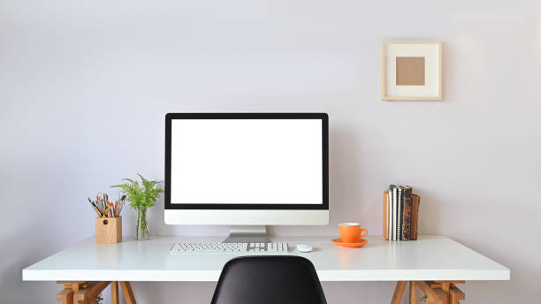 istock Computer monitor with white blank screen putting on working desk with wireless mouse, keyboard, pencil holder, stack of books, coffee cup and potted plant over white wall as background. 1217806832