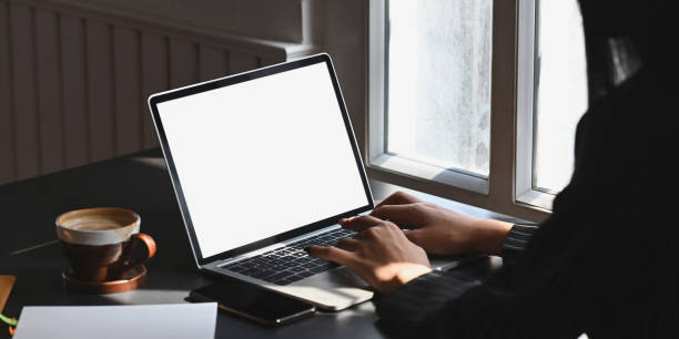 istock Photo of creative woman's hands typing on white blank screen computer laptop that putting together with coffee cup on black working desk while sitting in modern living room. Orderly workplace concept. 1217806968