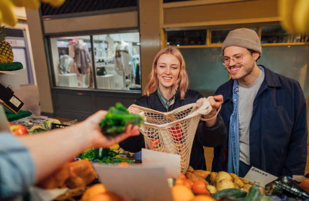 Shopping at the Market Point of view of a greengrocers owner giving a woman vegetables to put into a reusable bag. She is out shopping with her boyfriend. local products stock pictures, royalty-free photos & images