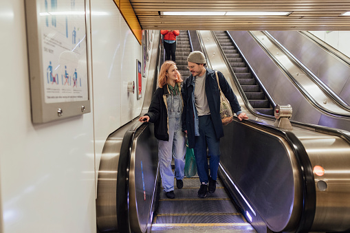 Couple walking through a subway station. They are on an escalator.