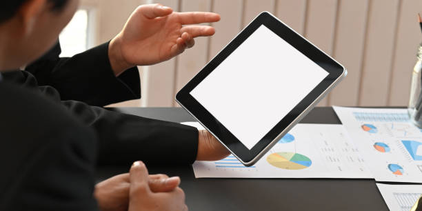 istock Cropped image of business people working together with computer tablet and graphic charts while sitting together at black meeting table over modern office as background. 1217807065