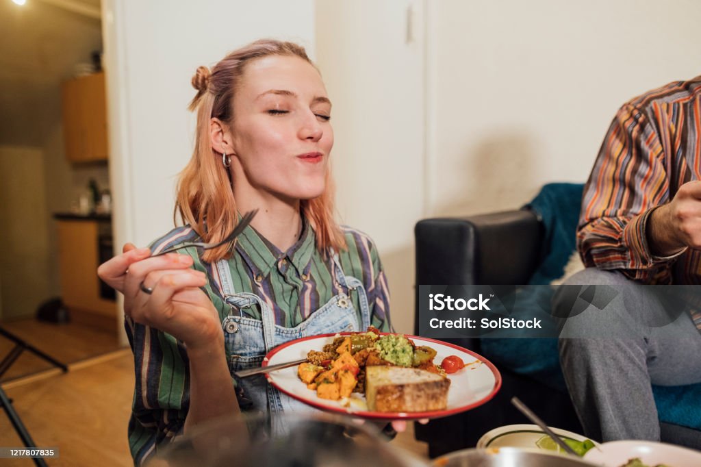 This is Delicious! Woman eating a home made vegan dish. Her and her friends have cooked creole aubergines and quinoa with sweet potatoes, peppers and avocado puree. She has her eyes closed and is enjoying the meal. Eating Stock Photo