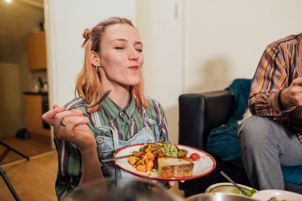 This is Delicious! Woman eating a home made vegan dish. Her and her friends have cooked creole aubergines and quinoa with sweet potatoes, peppers and avocado puree. She has her eyes closed and is enjoying the meal. veganism stock pictures, royalty-free photos & images
