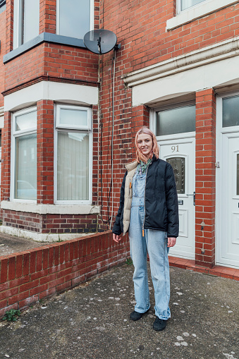 Woman wearing dungarees looking at the camera and smiling while standing at her front door.