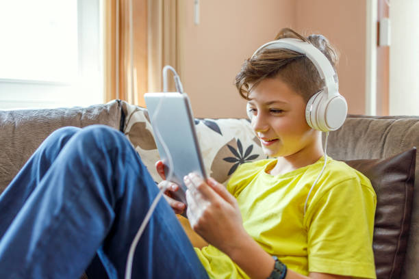 istock Joyful boy holding digital tablet when wearing headphones 1217811017