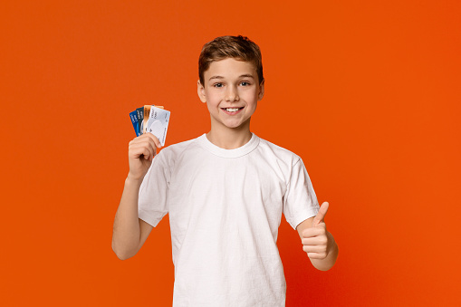 Cashless payments only. Teenage boy with lots of credit cards showing like gesture, orange studio background
