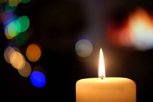 Photo of Burning white candle on a dark background with bokeh lights.