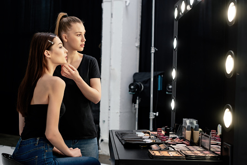 makeup artist touching face of attractive model and looking at mirror