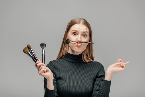 funny makeup artist holding cosmetic brushes isolated on grey