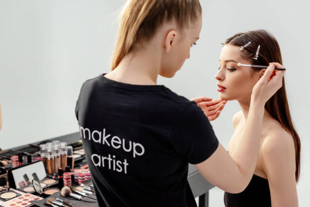 mujer en camiseta negra con el maquillador de letras de artista aplicando sombra de ojos en el modelo - makeup artist fotografías e imágenes de stock