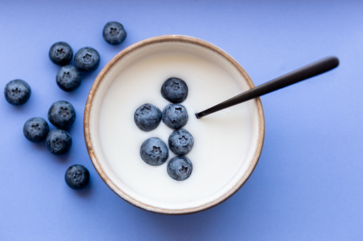 Healthy bowl of yogurt with blueberries and spoon on blue/purple background