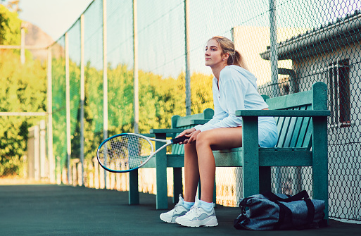 Shot of a sporty young woman sitting on a bench on a tennis court